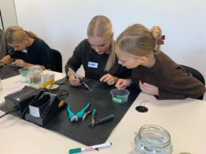 Jugendliche löten im Workshop in Wien an elektronischen Bauteilen auf einer Werkunterlage.